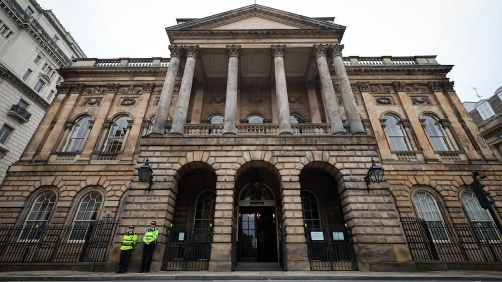 An old grand brick building with two police officers standing out the front. 