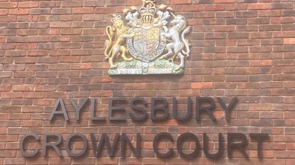 Sign for Aylesbury Crown Court: a red-brick wall containing the words AYLESBURY COURT COURT below a crest featuring a lion and a unicorn