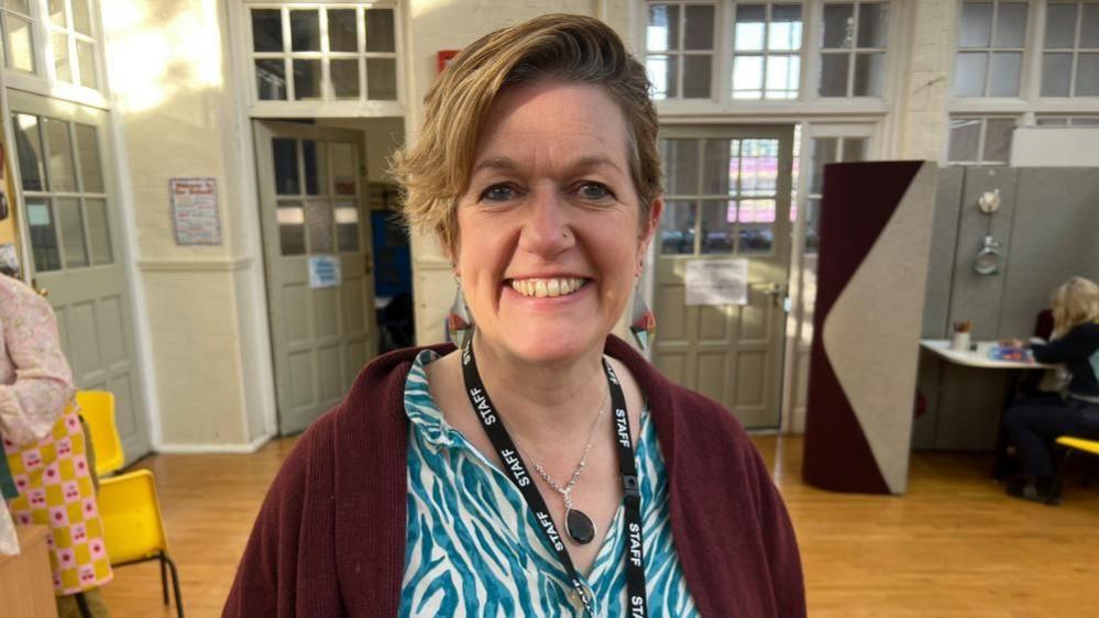 A woman with short blondish hair wears a black lanyard which reads staff