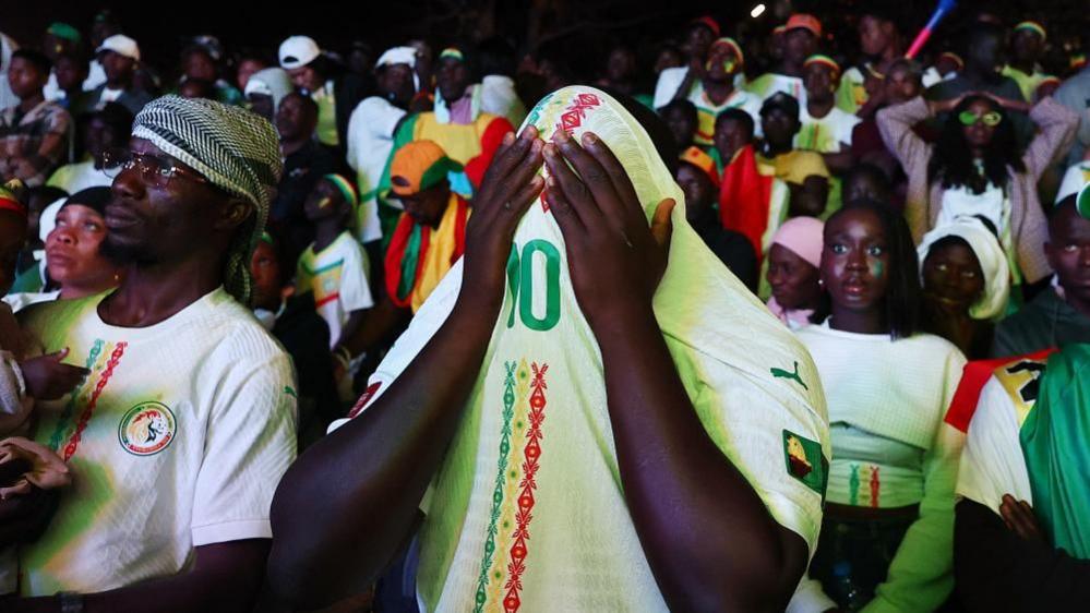 A Senegal fan covers his face with his football top printed with the number 10 on it.