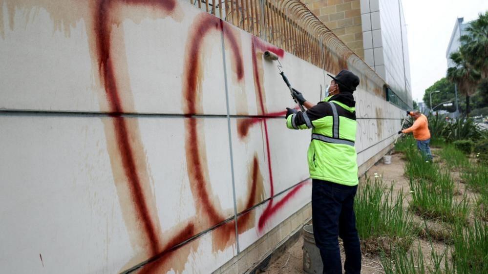 Workers clean up graffiti on the detention center building, after days of protests against federal immigration sweeps and the deployment of the California National Guard and US Marines, in Los Angeles