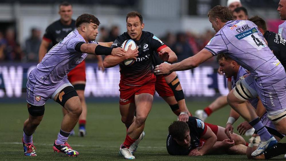 Saracens' Ivan van Zyl runs with the ball in his right hand as a Gloucester player (left) stretches his arms out towards him in an attempt to tackle