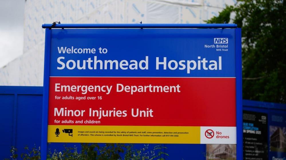 The photo shows a sign reading "welcome to Southmead Hospital". Underneath that part of the sign, which is blue, a red section highlights the presence of an "Emergency Department for adults aged over 16" and a "Minor Injuries Unit for adults and children".