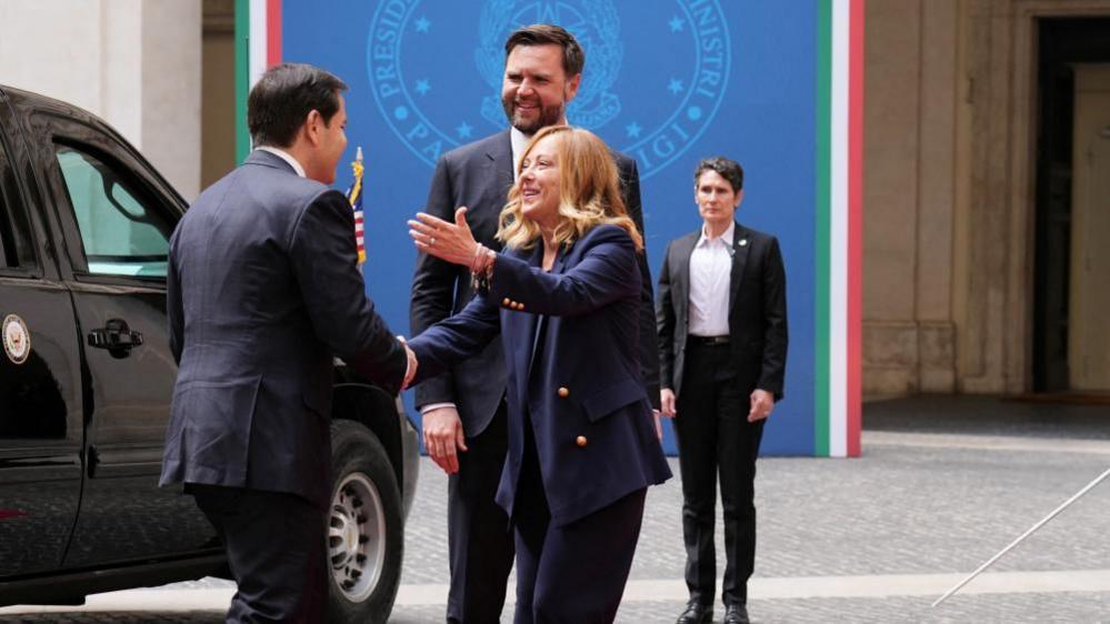 Italy's prime minister wears a blue suit as she greets US officials arriving in a black car in Rome