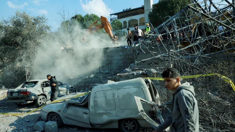 young men are seen near damaged cars at the site of an Israeli air strike near Byblos