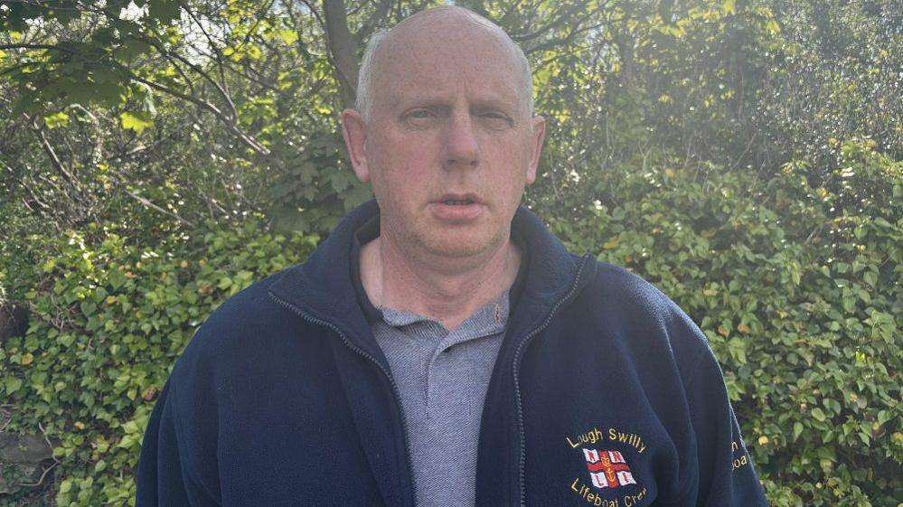 Joe Joyce, he has white hair and wearing a navy jacket that says Lough Swilly Lifeboat crew. He is wearing a grey polo shirt.