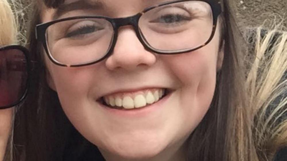 Georgina Callander, with long brown hair and wearing dark brown glasses, smiles as she poses for a photograph.