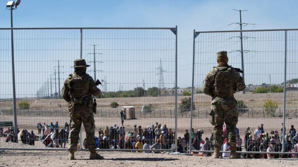 US soldiers watch over a group of migrants waiting to be allowed by the authorities to go to a CBP processing centre in El Paso