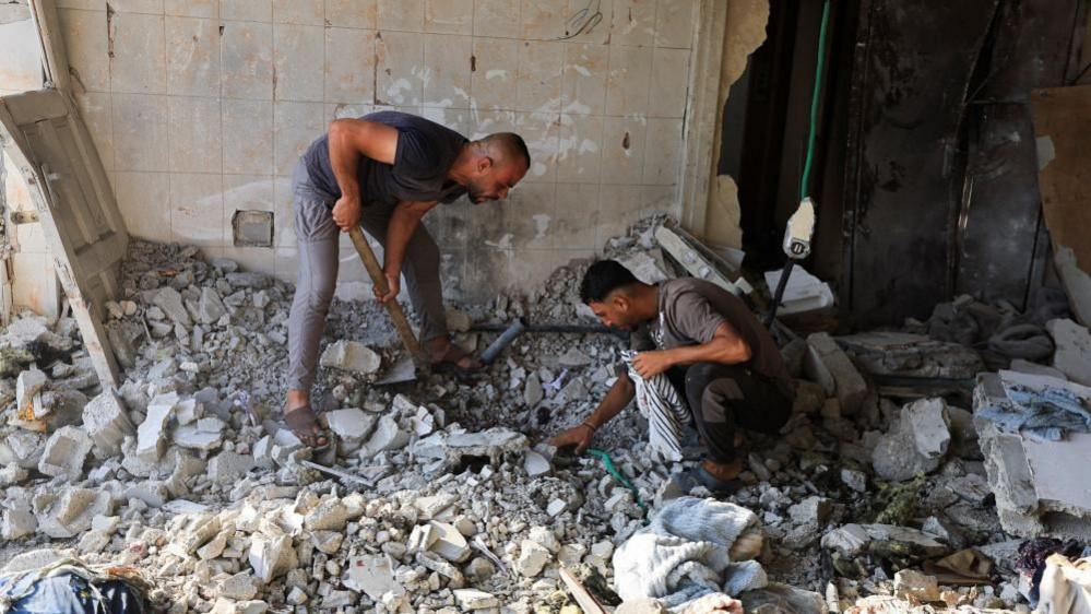 Two men search through rubble 