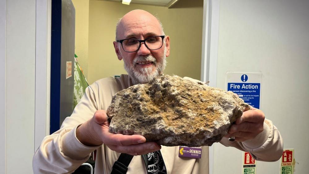Dennis Crunden holding the rock thrown through their charity shop window - roughly the size of a football.