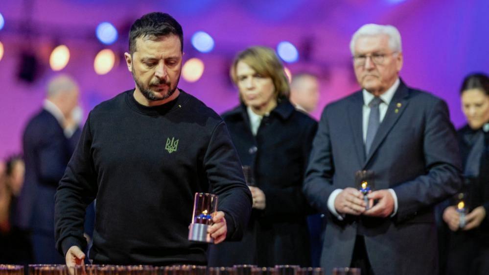 Zelensky, wearing a trademark dark top with a Ukrainian trident symbol, lights a candle inside the large tent during a ceremony at Birkenau