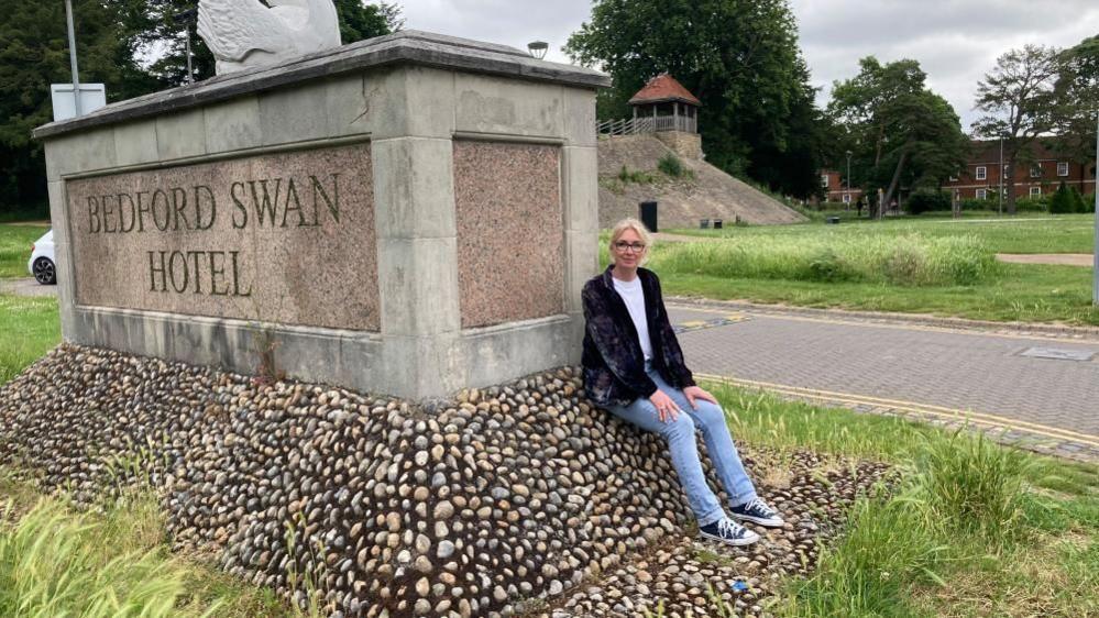 Ruth Hogan sitting on a hotel sign