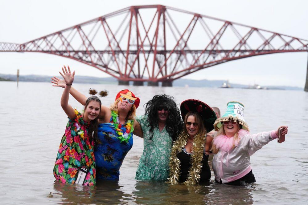 Five people in fancy dress stand hip-deep in the water in front of the Forth Rail Bridge.