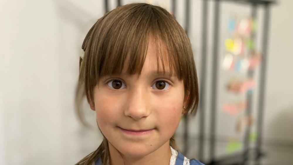 Alisa, an 8 year old girl with brown hair and a fringe, looks directly at the camera.