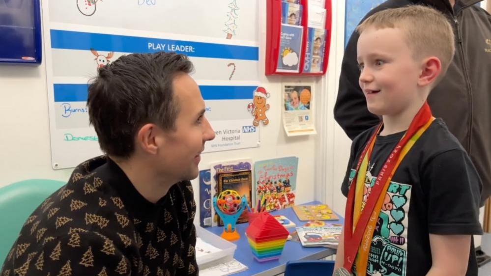 Multi-medal winning Paralympic table tennis player Will Bayley shows his medals to a young hospital patient in Brighton. 