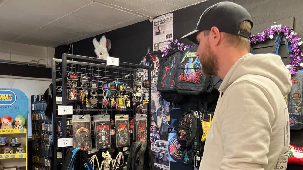 Man in hoodie and cap looking at film and horror merchandise displayed