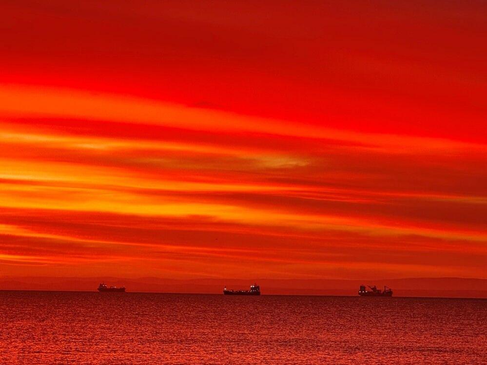 Three ships float on the water. The entire picture is covered in red light.