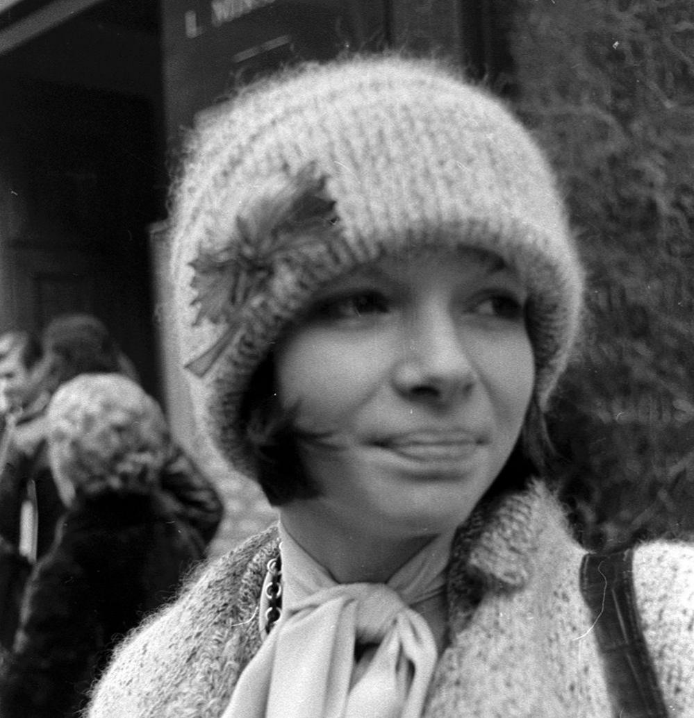 A black and white headshot image of a young Anna Wintour wearing a woollen hat, cardigan and a scarf