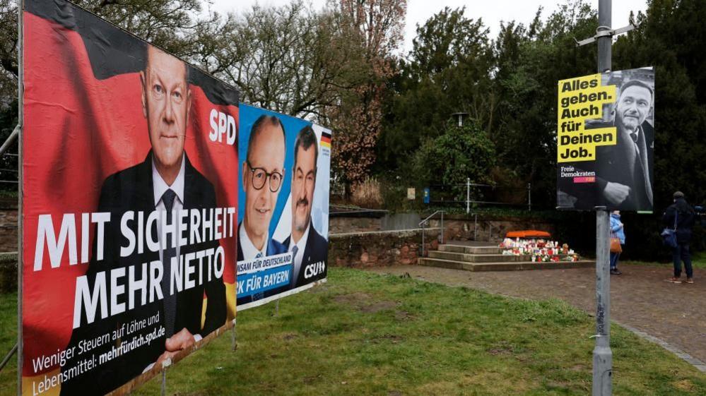 Election posters for Germany's chancellor and the main frontrunner in the vote can be seen a few metres from flower and candles in the park.