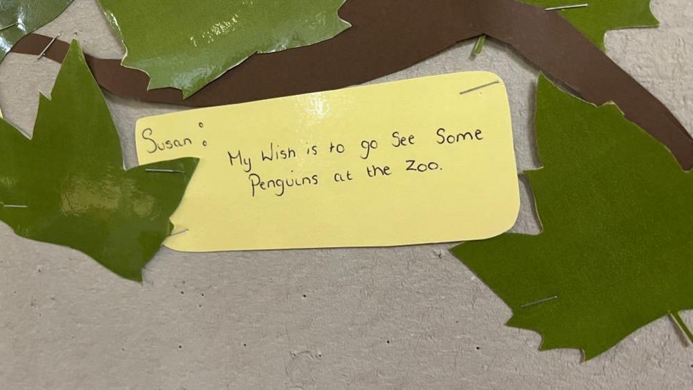 A yellow note on a noticeboard with Susan's wish, which reads: "My wish is to go see some penguins at the zoo."