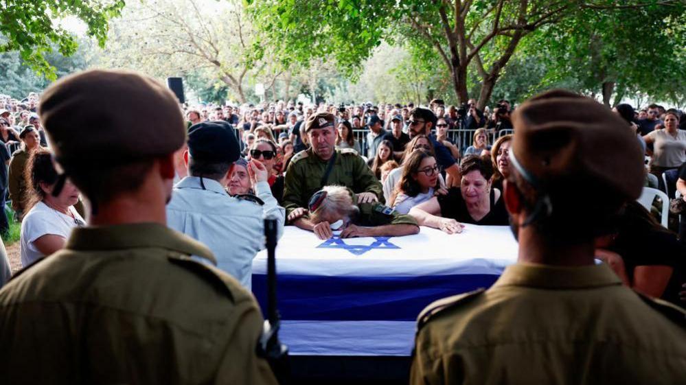 Large crowds gathered at funeral of Israeli soldier Sergeant Amitai Alon. Family members lean on his coffin crying with Israeli soldiers standing guard in front of it.