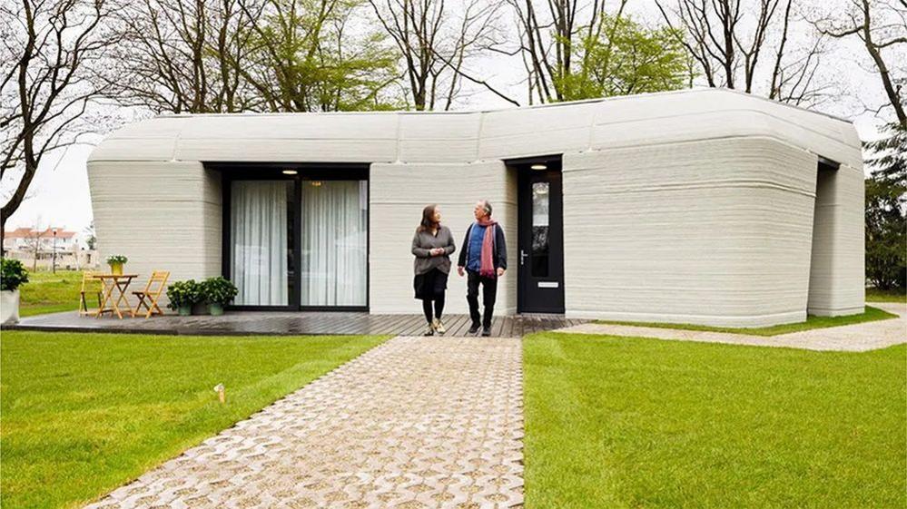 3d printed house with two people walking outside of it