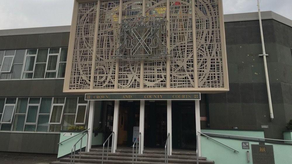 A two-storey building with a sign above the entrance reading: Plymouth Crown and County Courts. There are four entrance doors with steps leading up to them. Above the sign is a large decorative design of wrought stone work.