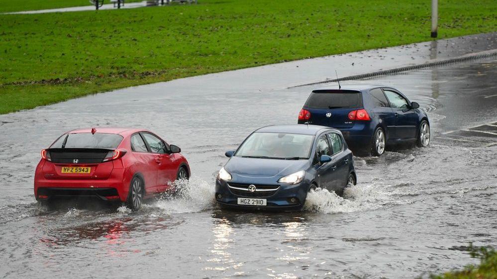 Three hatchback cars driving through flood water 