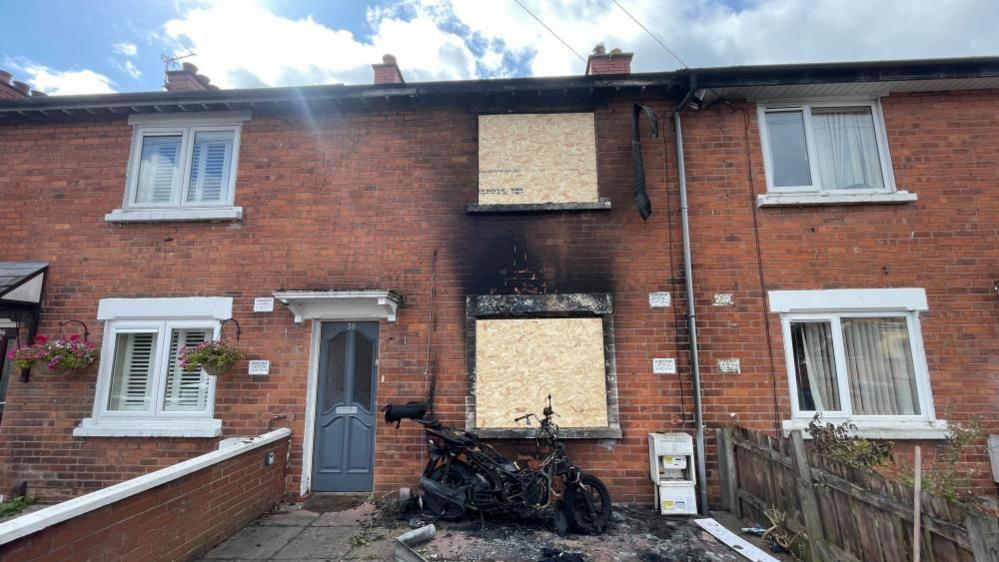 A destroyed motorcycle leans against the front of a house