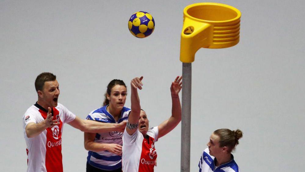 Four korfball players trying to score a goal.