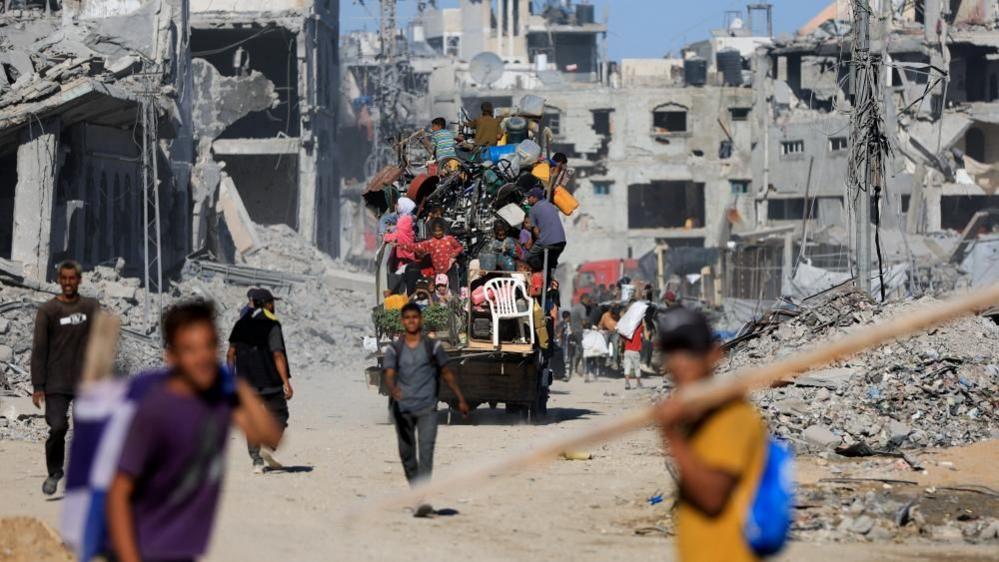 Palestinians on a vehicle pass by the rubble of destroyed buildings in Gaza City