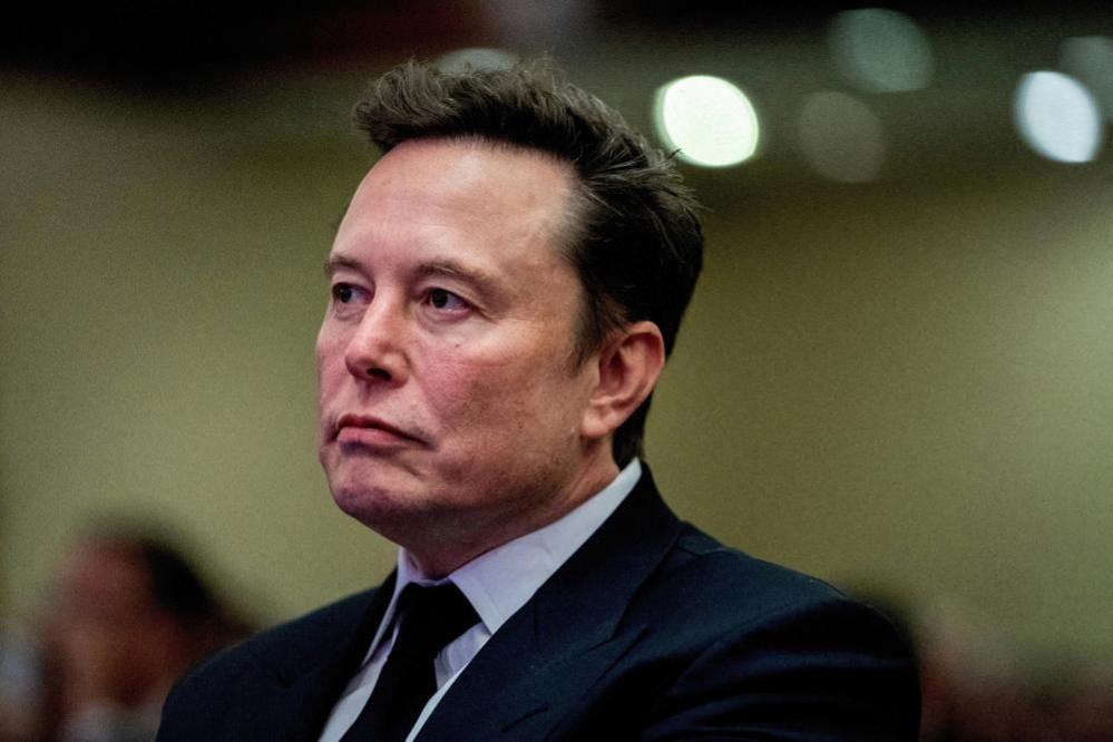 Tech billionaire Elon Musk. He is wearing a blue suit and tie and looking off to the left of the image. 