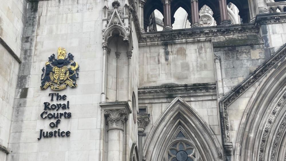 A grey stone building with the words "Royal Courts of Justice" written in black on the side of a wall.