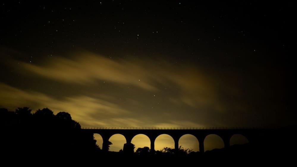 The Leaderfoot viaduct can be seen silhouetted against the night sky, a pale yellow glow near the horizon makes the bridge easy to see in the night.