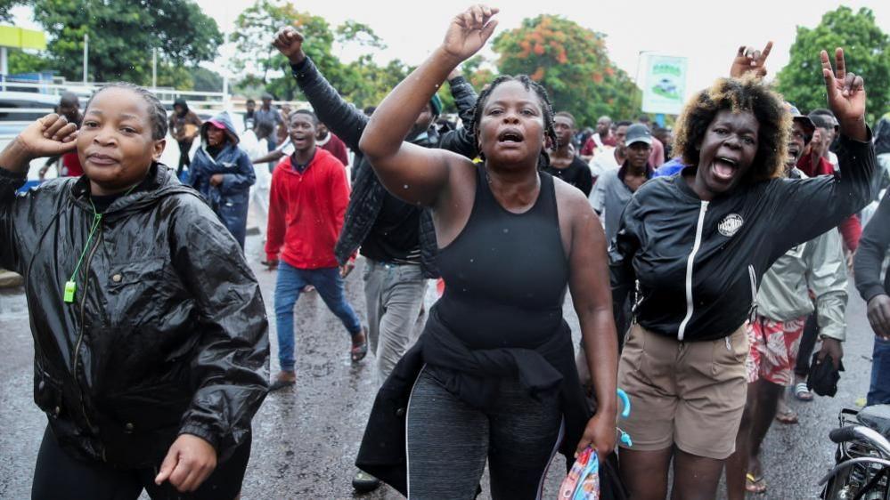 Women dressed in black hold their hands in the air as they wait to greet the Mozambican opposition leader 