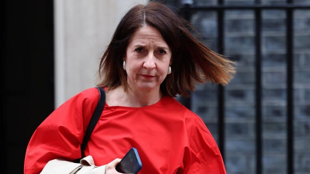 Liz Kendall leaving Downing Street on 11 March 2025. She is wearing a red top and carrying a phone in her right hand