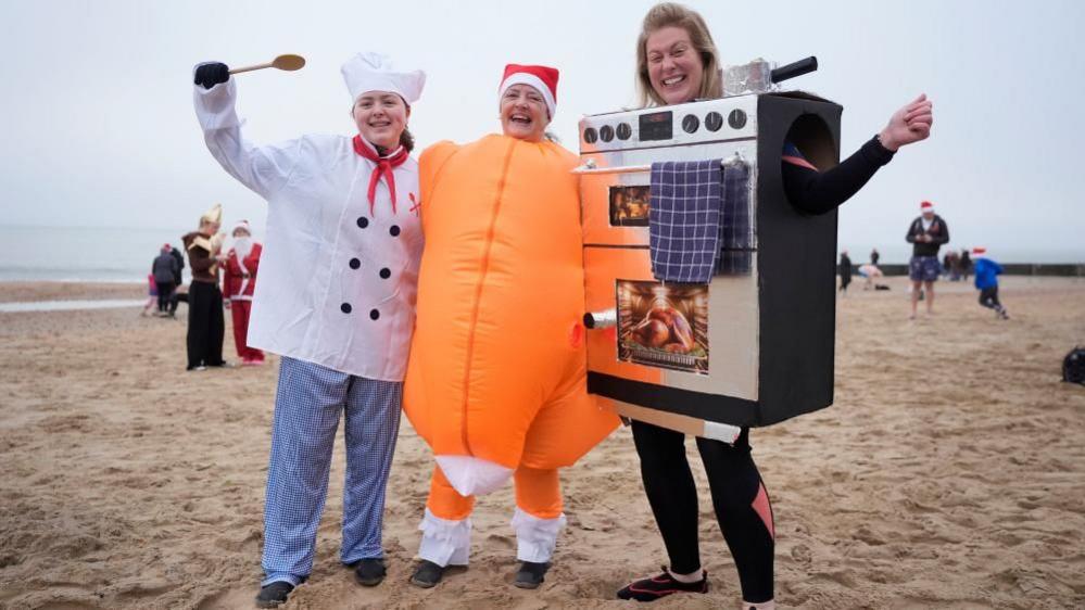 A woman dressed as a achef, next to a women dressed as a turkey while a third woman is dressed as an oven. 