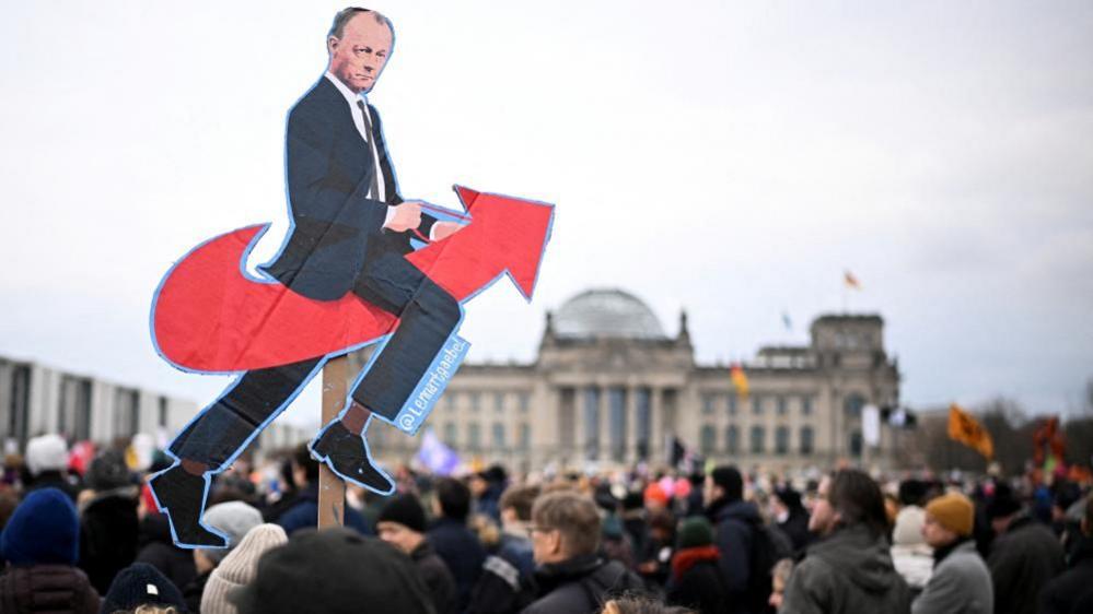 An effigy of Friedrich Merz riding a red arrow - the logo of the far right