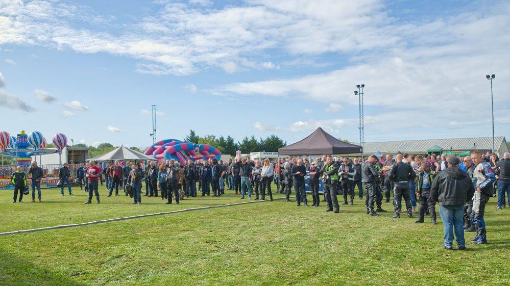 A group of people in a field with a set up for an event, including bouncy castle, gazebos and a fun fair ride