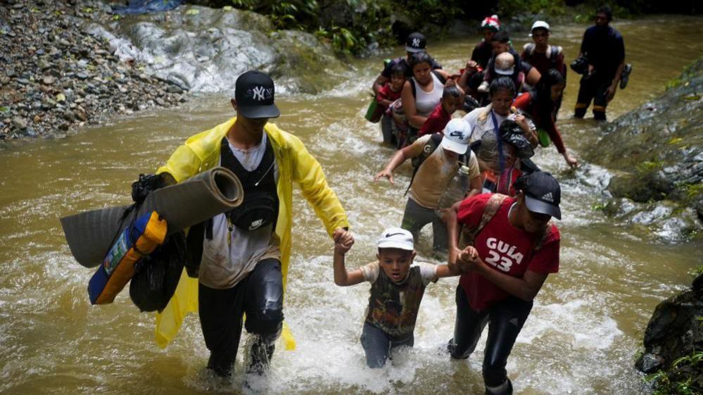 A group of people, including one young boy, wade through muddy water in the Darien gap