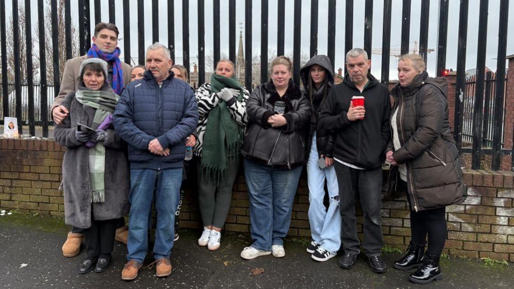 Gary's family stand huddled together in front of a grey steel fence, where the cyclist died. 