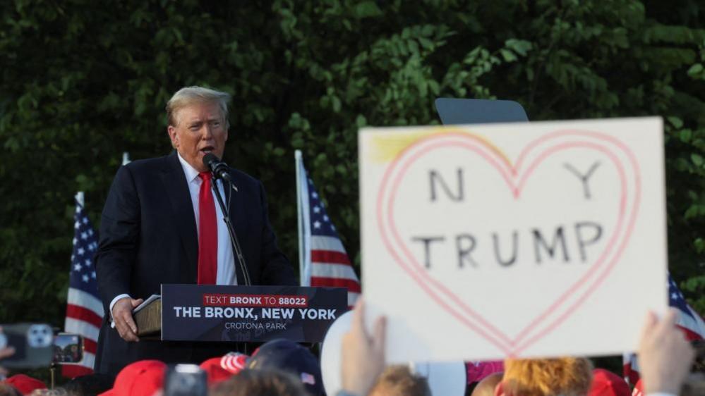 A person holds up a sign as former U.S. President and Republican presidential candidate Donald Trump speaks during a campaign rally at Crotona Park in the Bronx 