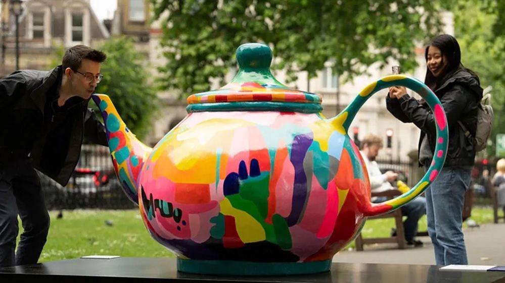 man posing next to giant teapot