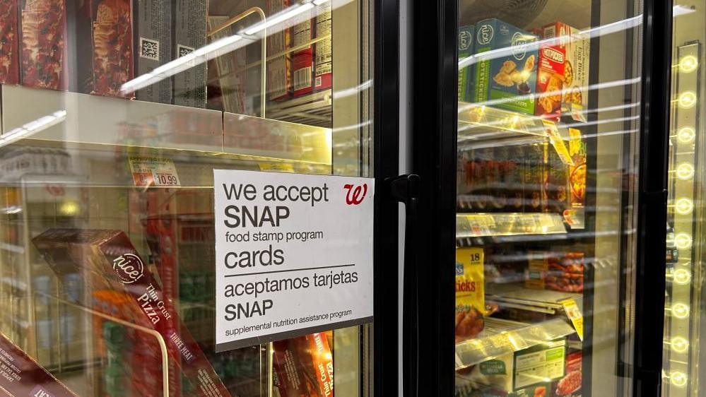 A frozen aisle in a grocery store shows a sign on the door reading "we accept Snap food stamp program cards".