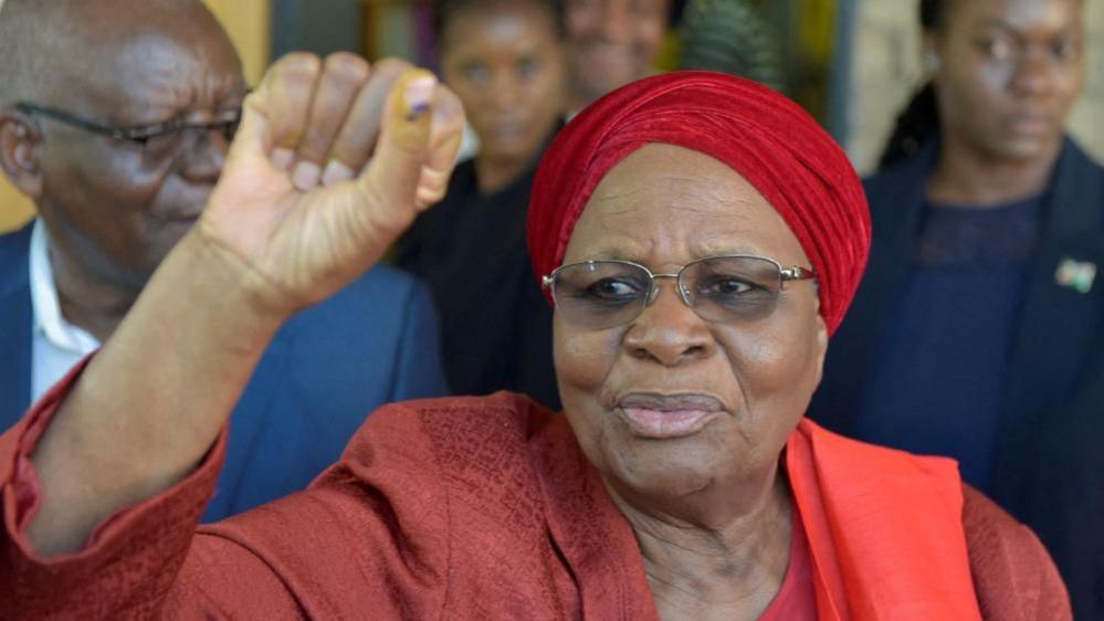 Netumbo Nandi-Ndaitwah wearing a red head wrap and suit raises her fist in a victory sign