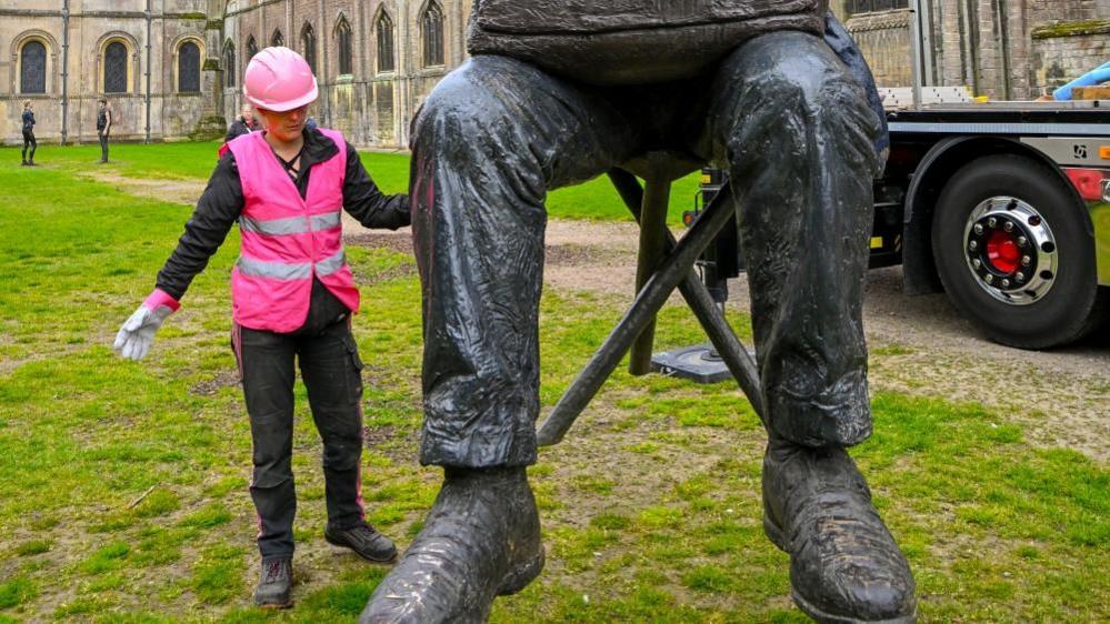 Woman manoeuvring feet of exhibit into place at Ely Cathedral 