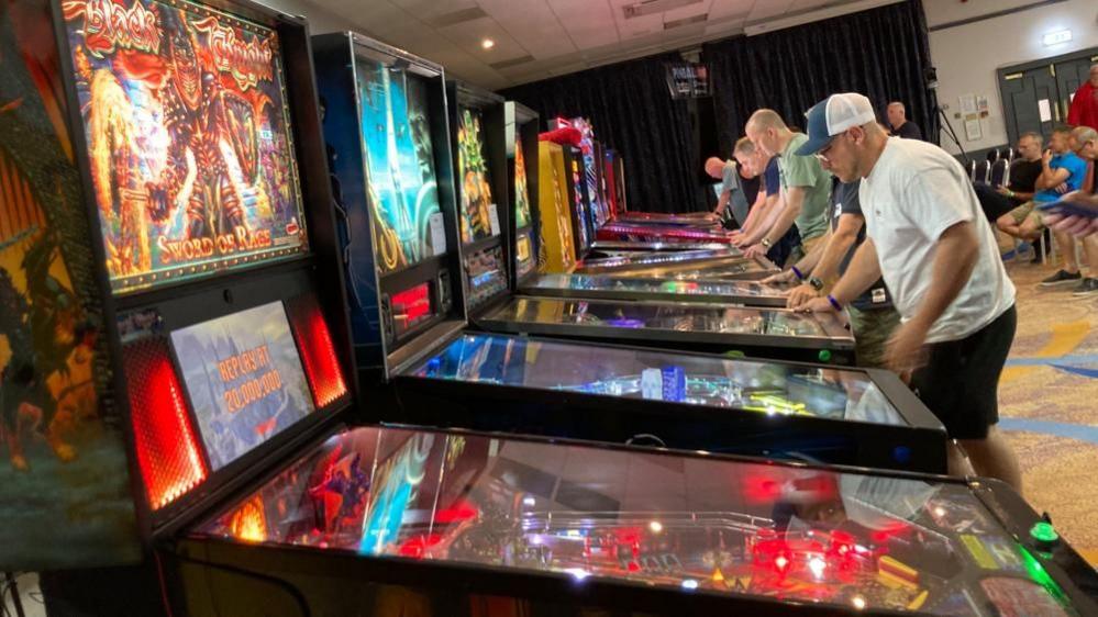 Line of pinball machines with people playing some of them