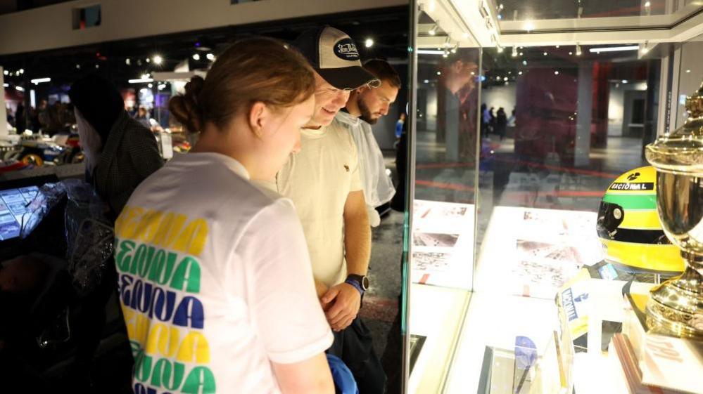 Two people looking into a glass case with a trophy and helmet inside.