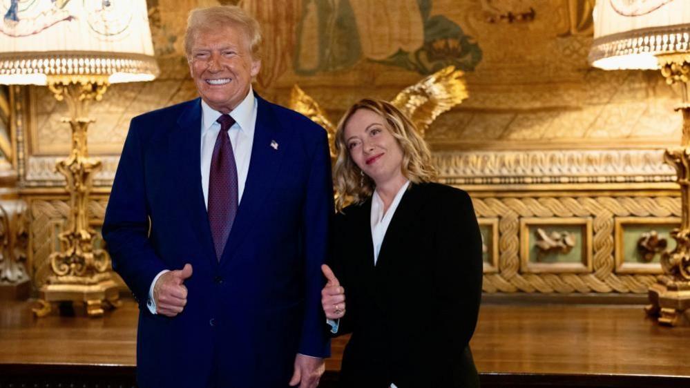 Italy's Giorgia Meloni stands beside Donald Trump holding her thumb in the air as they both smile