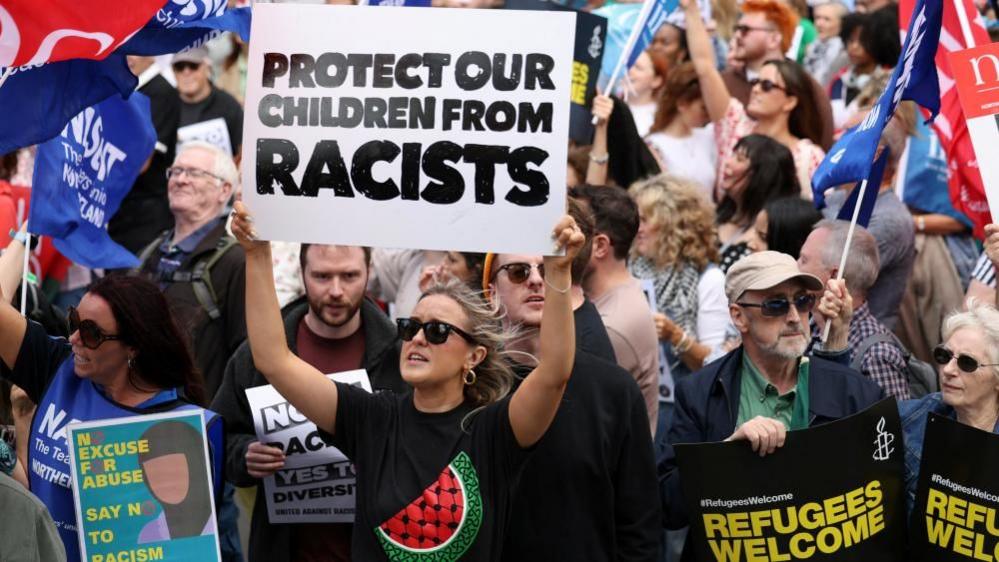 A woman in a crowd holds a sign that says protect our children from racists